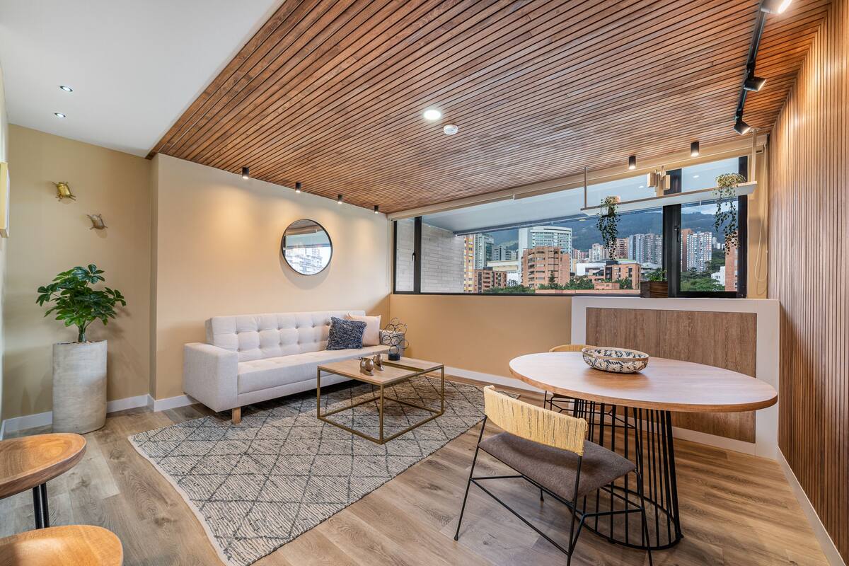 Una sala de estar moderna con un sofá blanco, una mesa de centro redonda y un comedor con mesa y sillas de madera.
