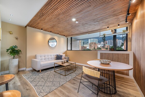 Een moderne woonkamer met een witte bank, een ronde salontafel, en een eethoek met een houten tafel en stoelen.