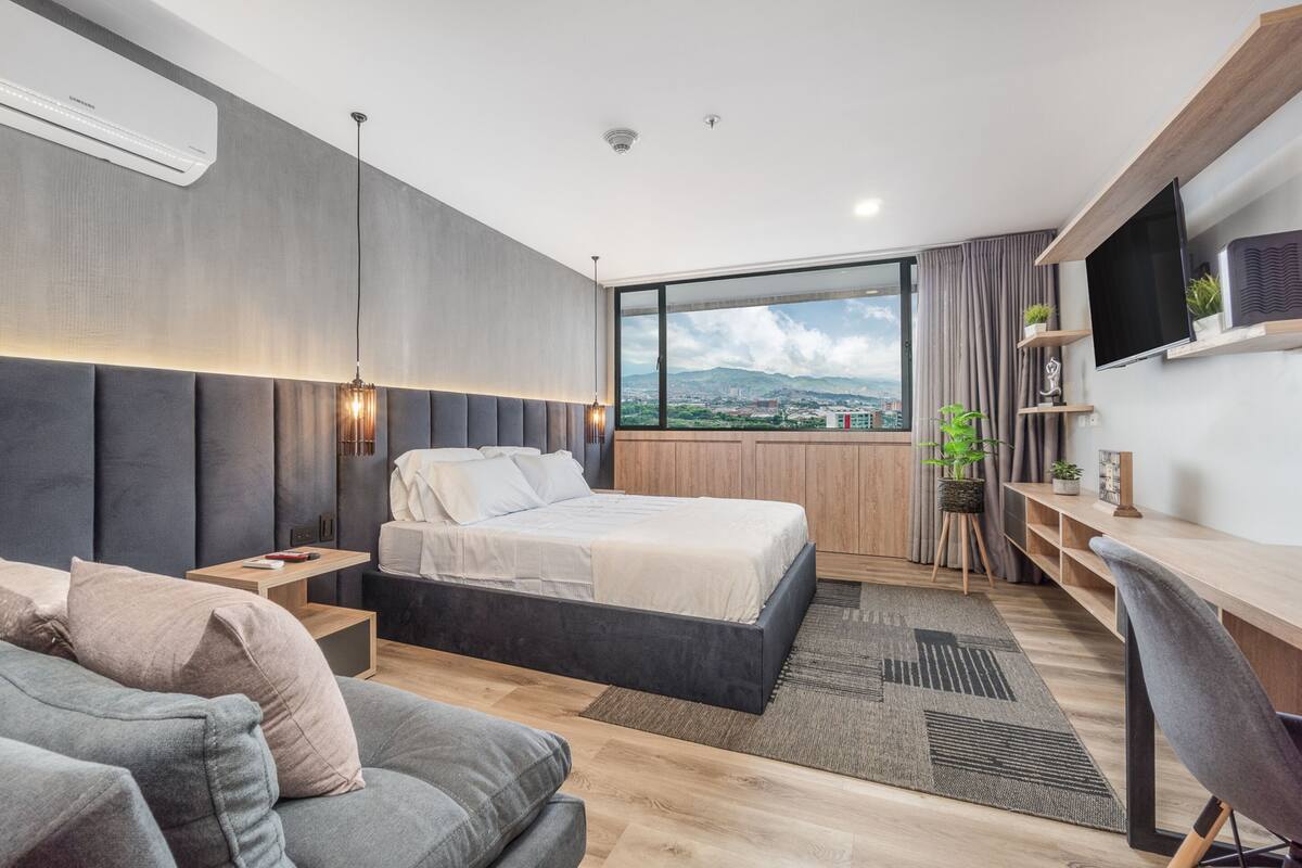 Un dormitorio moderno con una cama grande, un escritorio, un sofá y vistas a la ciudad.