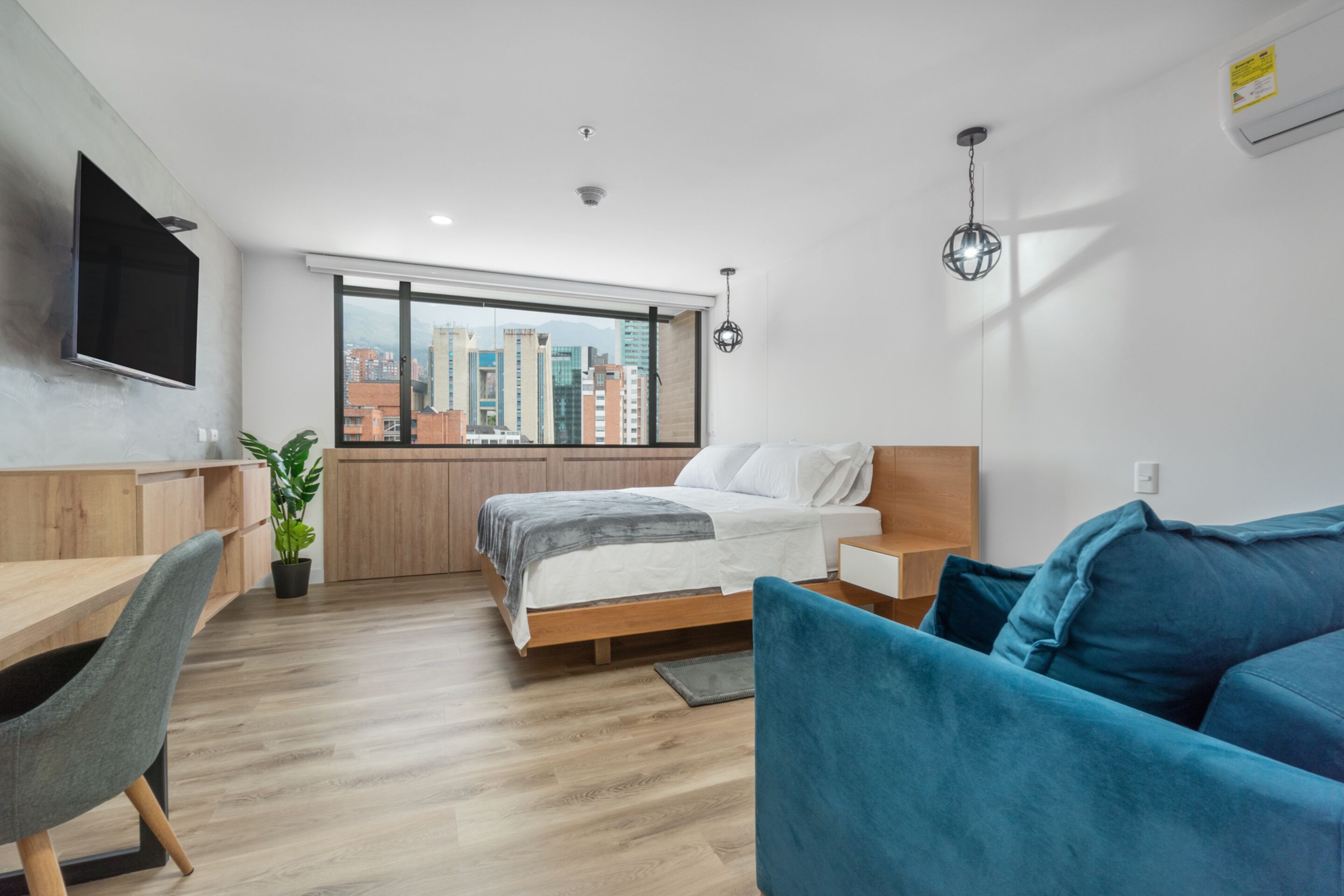 Een moderne hotelkamer met een bed, een bureau, een televisie en een groot raam met uitzicht over de stad.