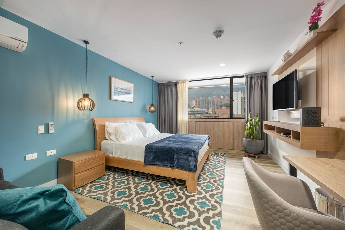 Una habitación de hotel moderna con cama, mesita de noche, televisión y vistas a la ciudad.