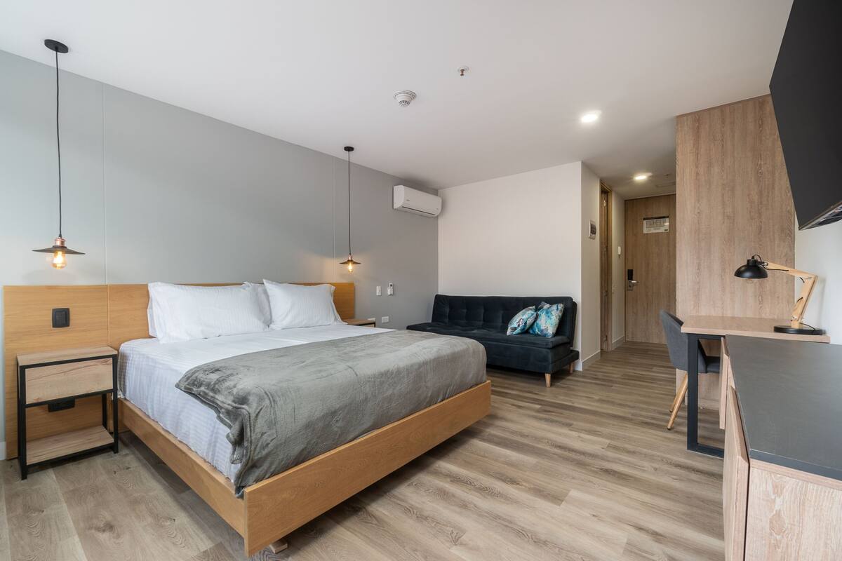 Un dormitorio moderno con una cama de madera, mesitas de noche, un escritorio y un sofá oscuro.