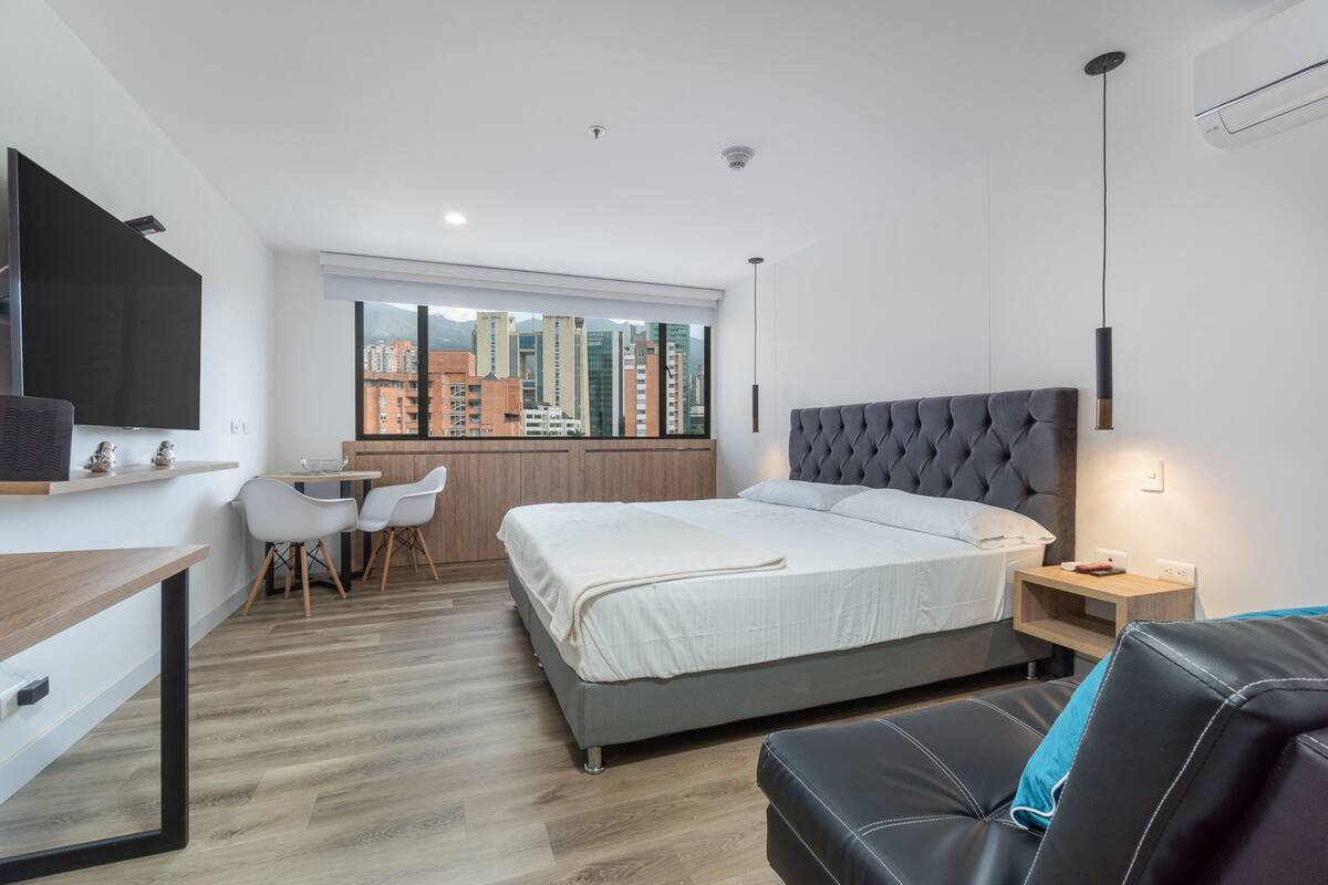 Un dormitorio moderno con una cama grande, un escritorio y vistas de la ciudad a través de amplios ventanales.