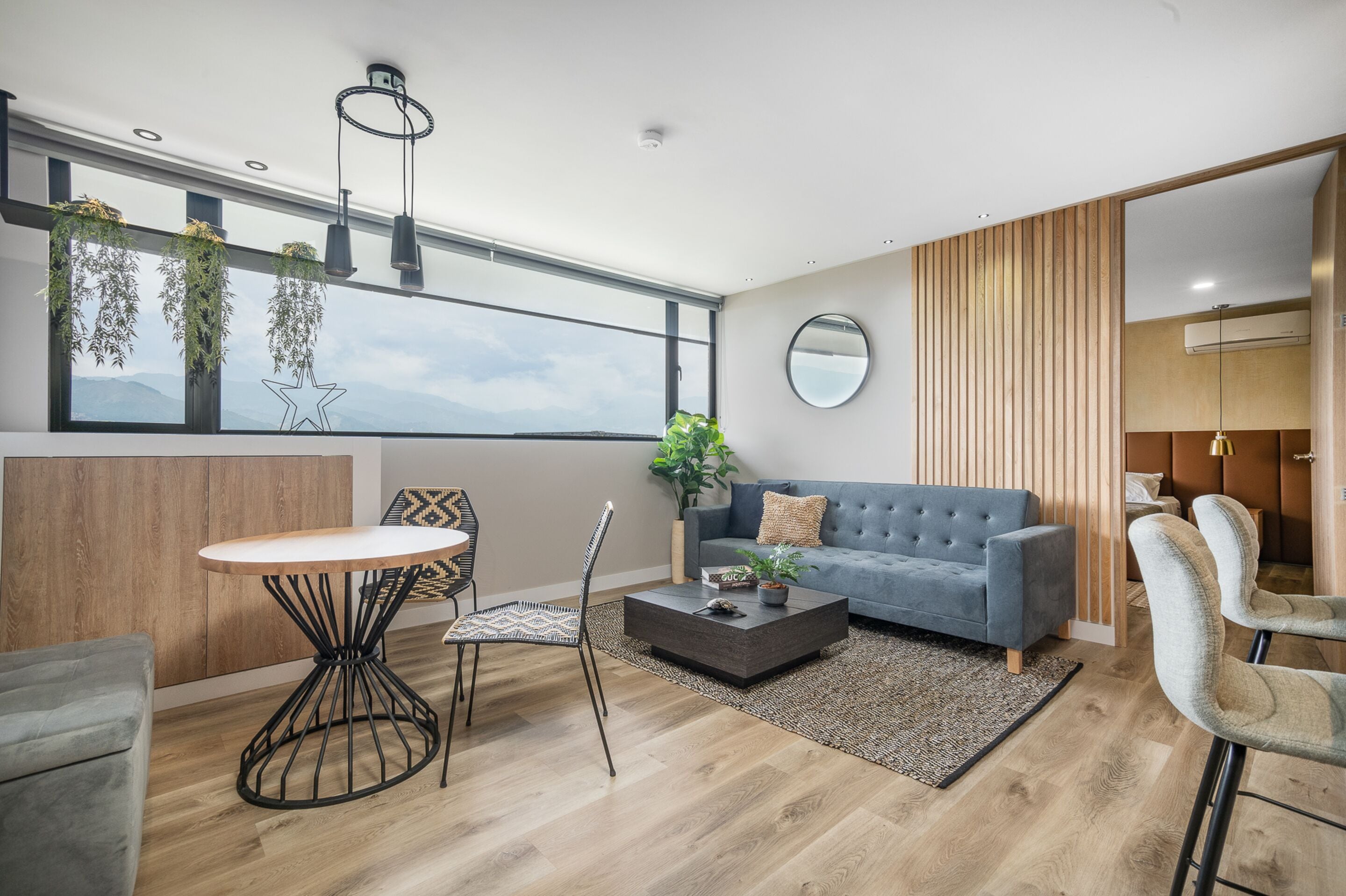 Een moderne woonkamer met een grijze bank, een ronde salontafel, en een eethoek met een witte tafel en zwarte stoelen.