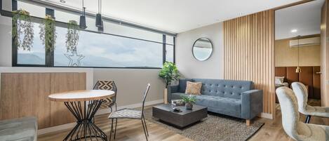 A modern living room with a grey sofa, a round coffee table, and a dining area with a white table and black chairs.
