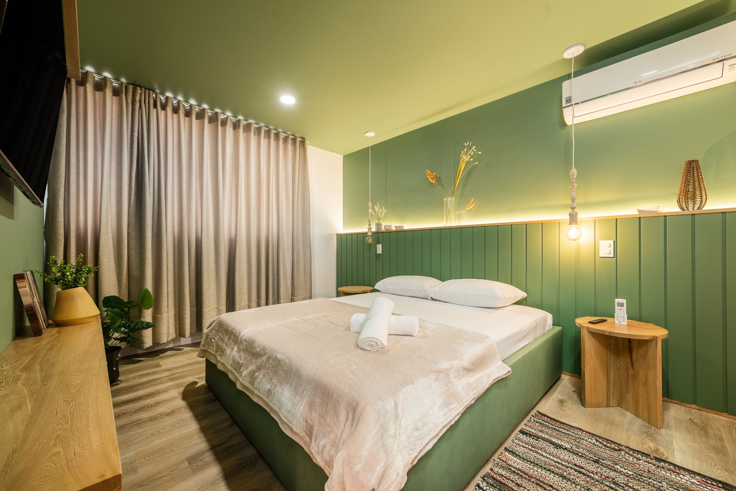 A neatly made bed with a rolled towel, a bedside table with a lamp, and a wall-mounted air conditioner.