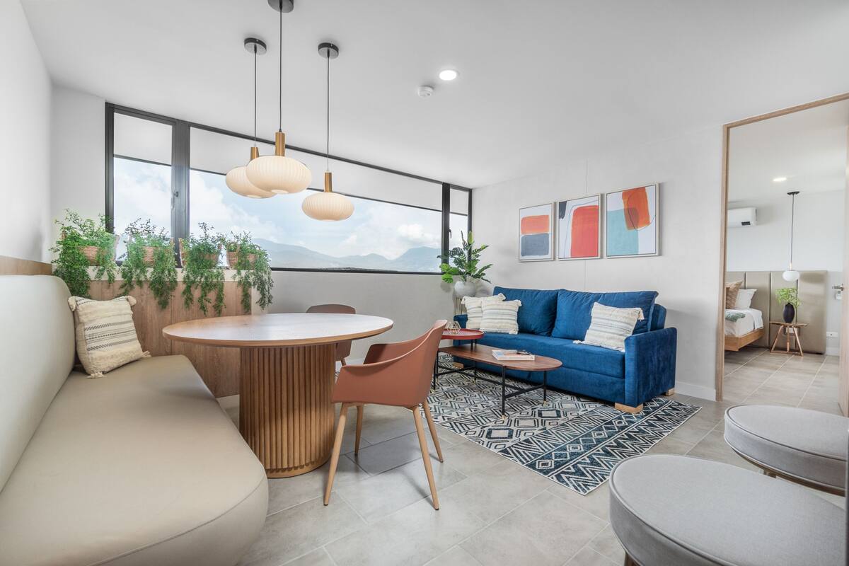 Un salón moderno con una mesa redonda de madera, un sofá azul y una alfombra estampada.