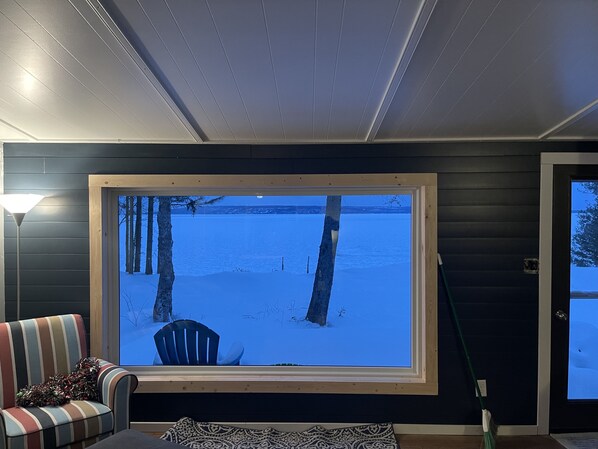 A room with a large window overlooking a snowy landscape, a chair, a lamp, and a broom.