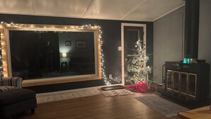 Una sala de estar acogedora con un ventanal grande, un pequeño árbol de Navidad, una chimenea y una pared de color oscuro.