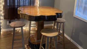 Un comedor con una mesa de madera, dos taburetes, una lámpara colgante y una ventana con cortinas.