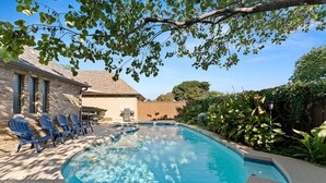 A swimming pool with blue water, surrounded by a stone patio and blue chairs. - Luxury Home Sleeps 20 with Heated Pool & Billiard (Dallas)