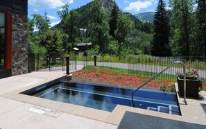 A swimming pool with a stone wall, surrounded by a fence, and a mountain view in the background.