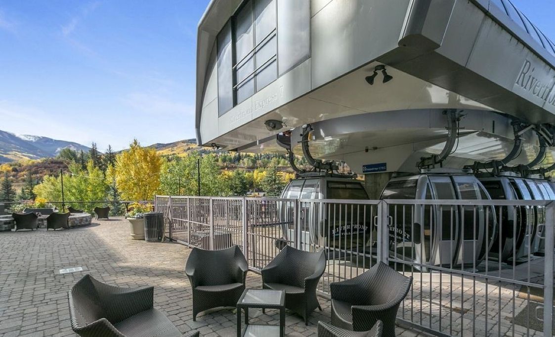 Un bâtiment moderne doté d’un espace extérieur aménagé, abrité et agrémenté de meubles en osier, offrant une vue sur les montagnes.