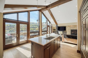 A modern kitchen with large windows, a central island, and a stone fireplace.