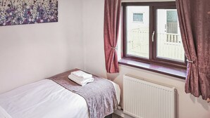 Ein Schlafzimmer mit einem Bett, einem Fenster mit Vorhängen, einem Heizkörper und einer Wand mit einem floralen Gemälde.