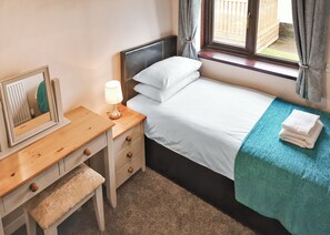 A bedroom with a bed, bedside table, lamp, mirror, and a window with curtains.