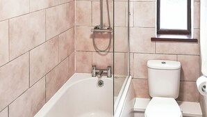 Et badeværelse med badekar, toilet og et vindue.