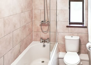 A bathroom with a bathtub, toilet, and a window.