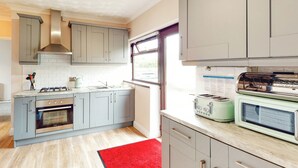 Et moderne køkken med lysegrå skabe, en rød måtte, indbygget ovn, gasblus og en vintage-toaster.