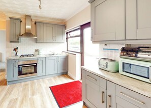 A modern kitchen with grey cabinets, a red rug, a built-in oven, a gas stove, and a vintage toaster.