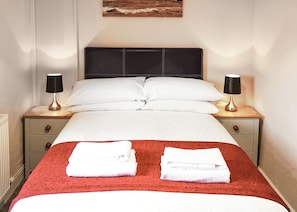 A neatly made bed with white linens, two bedside lamps, and a red throw blanket.