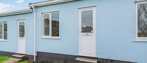 A row of blue mobile homes with numbered doors, a grassy yard, and a clear sky.