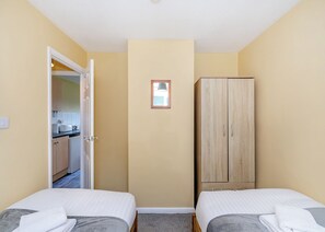 Ein kleines Zimmer mit zwei Betten, einem Kleiderschrank, einer Tür zu einer Küchenzeile und einem kleinen Fenster.