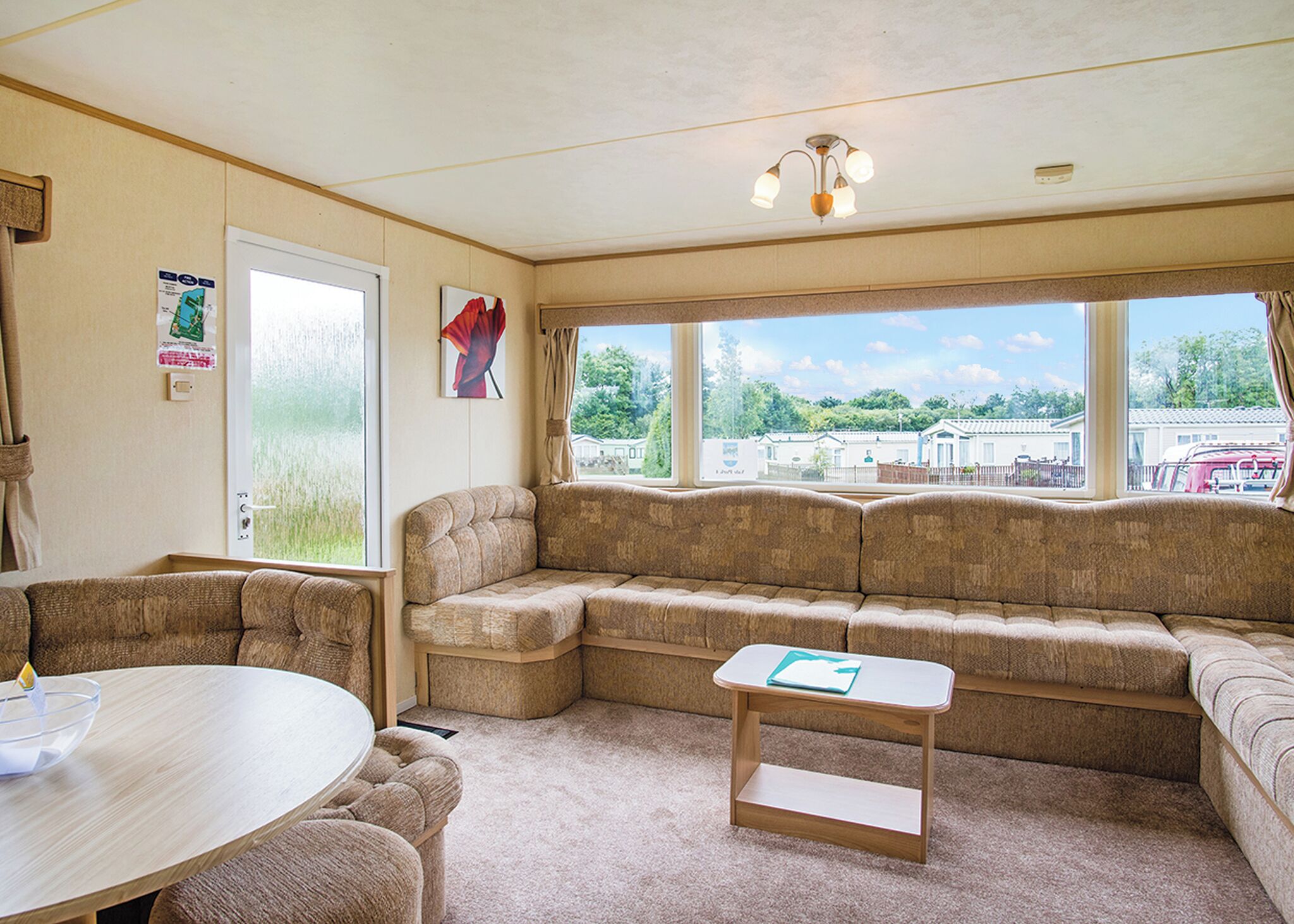 A cozy living room with a sectional sofa, a small table, and a view of a residential area through large windows.