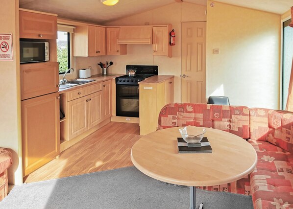 A compact kitchen with wooden cabinets, a microwave, stove, and a sink. There's a round table with a bowl and a laptop.