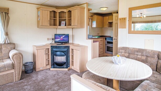 A compact RV interior with a kitchenette, a television, a seating area, and a small table. - Comfortable and spacious 12ft-wide caravan with one double and two twin. (Ludchurch, Nr Saundersfoot)