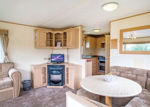 A compact RV interior with a kitchenette, a television, a seating area, and a small table.