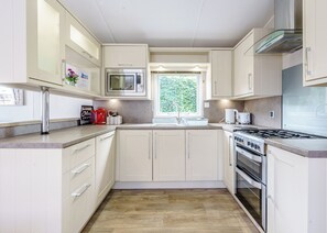 Une cuisine moderne avec des meubles blancs, un four à micro-ondes encastré, une cuisinière à gaz et une fenêtre laissant entrer la lumière naturelle.