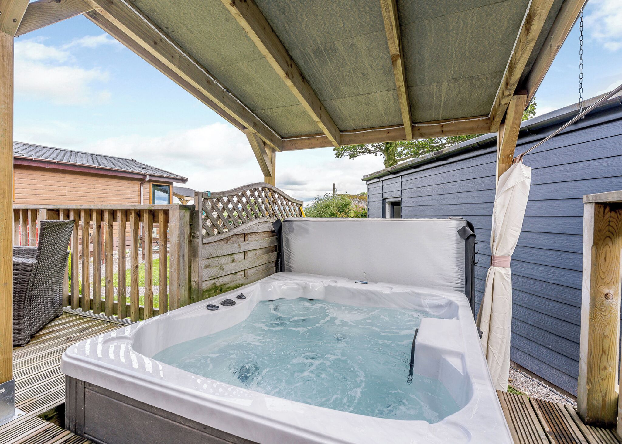 A hot tub under a wooden pergola with a wooden deck and a house in the background.
