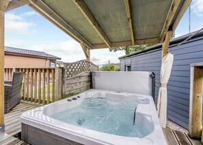 Un bain à remous sous une pergola en bois, avec une terrasse en bois et une maison en arrière-plan.