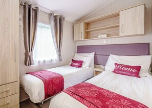 A bedroom with two beds, a wardrobe, a bedside table, and a window with curtains.