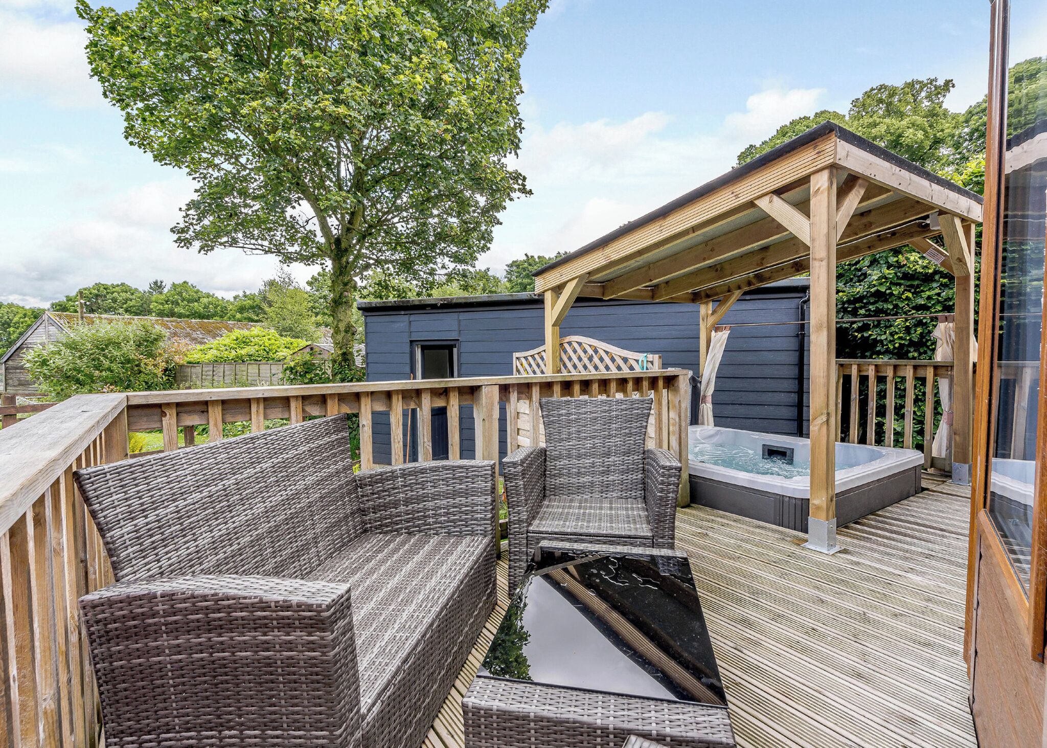 A deck with wicker furniture, a hot tub, and a wooden pergola.