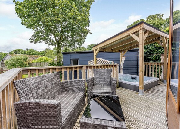 Une terrasse dotée de meubles en osier, d’un jacuzzi et d’une pergola en bois.