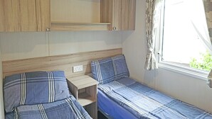 A compact RV interior with two sleeping areas, a small table, and a window with curtains.
