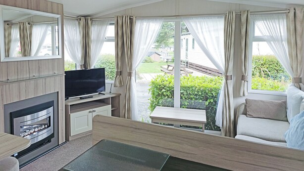 A modern RV interior with a television, fireplace, and seating area with a view of the outdoors.