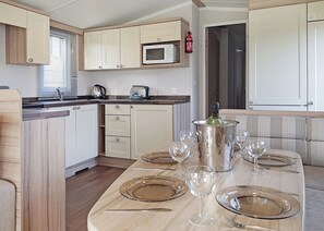 A compact kitchen with wooden cabinets, a microwave, and a dining area set for six with wine glasses and cutlery. - Modern caravan with one double and one twin. (Saundersfoot)