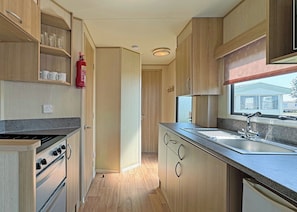 A compact kitchen with wooden cabinets, a gas stove, a sink, and a fire extinguisher.