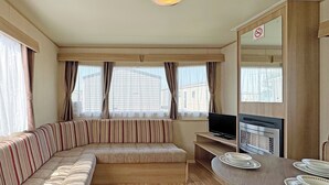 Ein kompakter Wohnbereich mit Sofa, Fernseher, Esstisch mit Tellern und einem Rauchverbot-Schild.