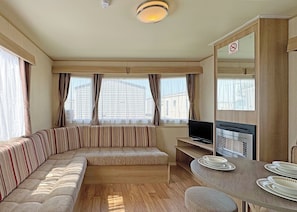 A compact living space with a sofa, a television, a dining table with plates, and a no-smoking sign.