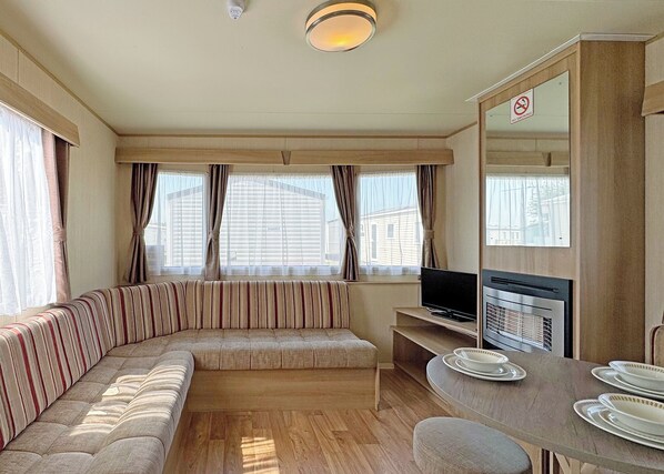 A compact living space with a sofa, a television, a dining table with plates, and a no-smoking sign.