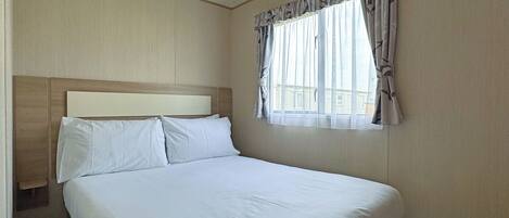 Une chambre d’hôtel avec un grand lit, une tête de lit, une fenêtre avec des rideaux et une vue sur les bâtiments environnants.