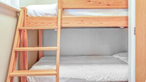 Una cama litera con escalera de madera, ropa de cama blanca y colchón gris.