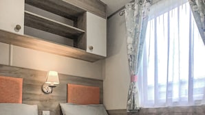 Ein Hotelzimmer mit Bett, Nachttisch, Wandregal, Fenster mit floralen Vorhängen und Wandlampe.