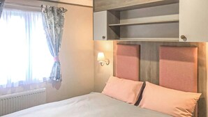 Ein Bett mit zwei Kissen, ein Nachttisch, eine Wandlampe und ein Fenster mit Vorhängen.