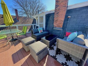 A covered outdoor patio with wicker furniture, a glass table, and a yellow umbrella. - The Loft at Charlotte's Rose (Charlottetown)