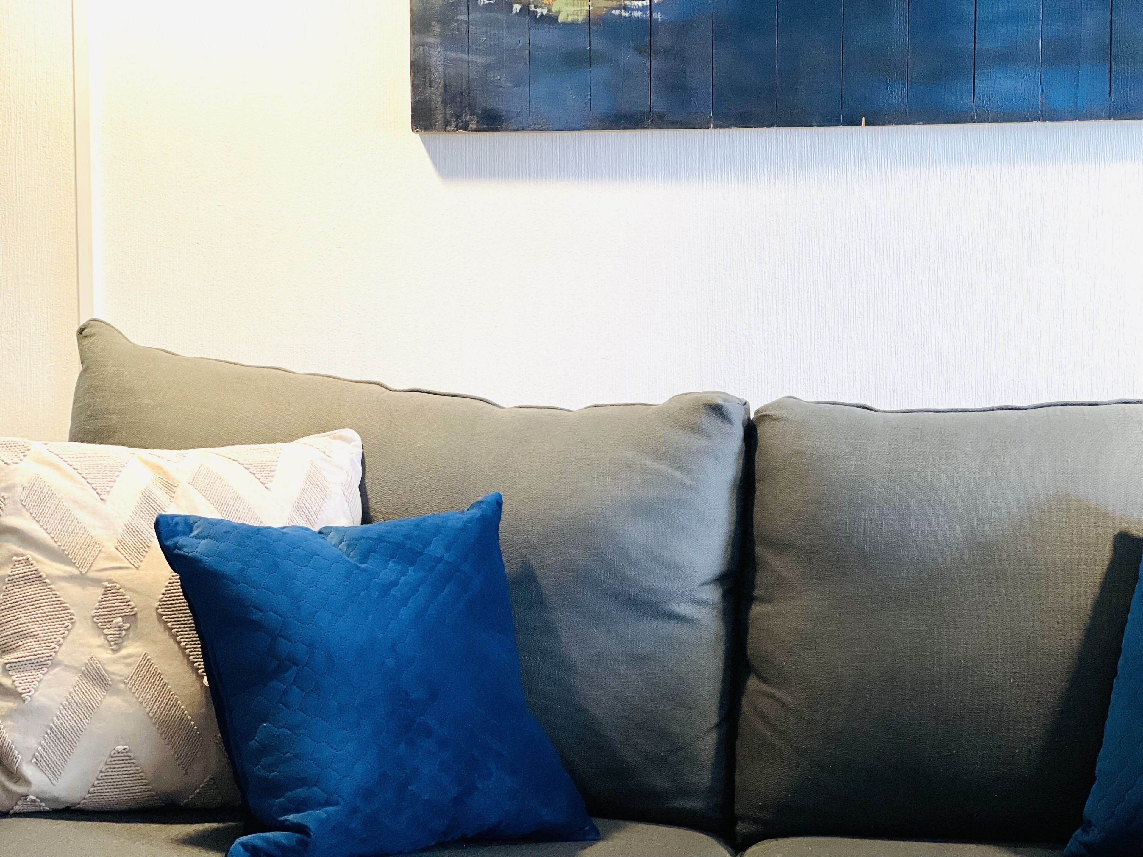 Un sofá gris con dos cojines, uno blanco y otro azul, frente a una pared lisa.